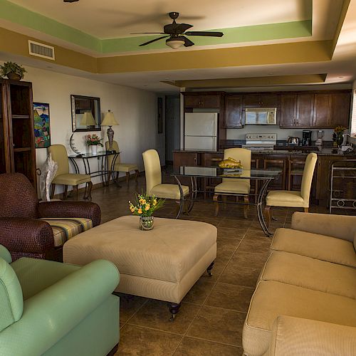 A spacious living area with a sofa, armchairs, a TV, and a kitchenette in the background. The atmosphere is cozy and inviting.