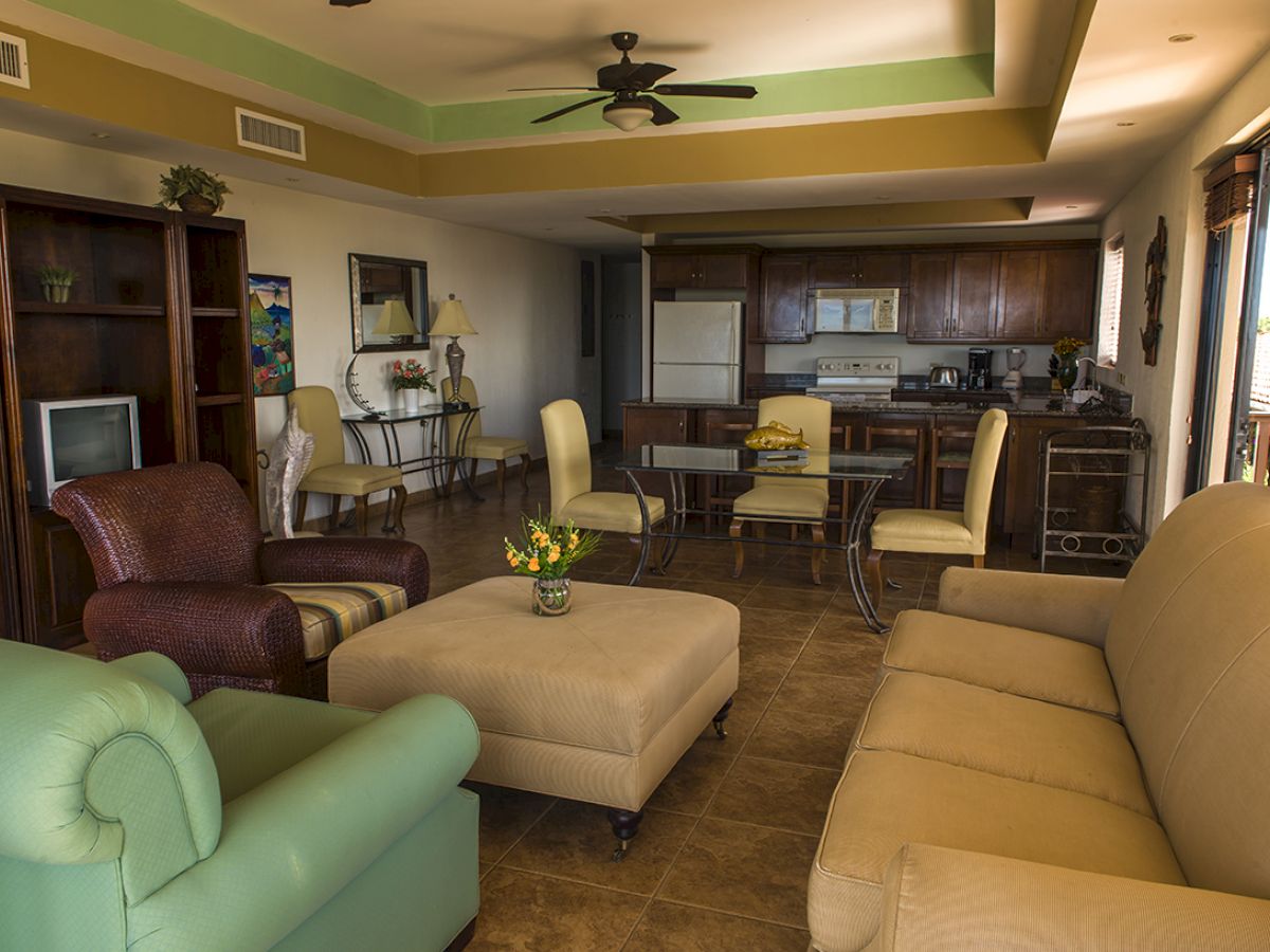 A cozy living room with assorted couches, a TV, and a dining area. The kitchen features dark wooden cabinets and modern appliances, ending the sentence.