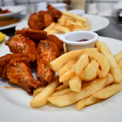 The image shows a plate of fried chicken wings and French fries with a small cup of dipping sauce on the side, all served on a white plate.