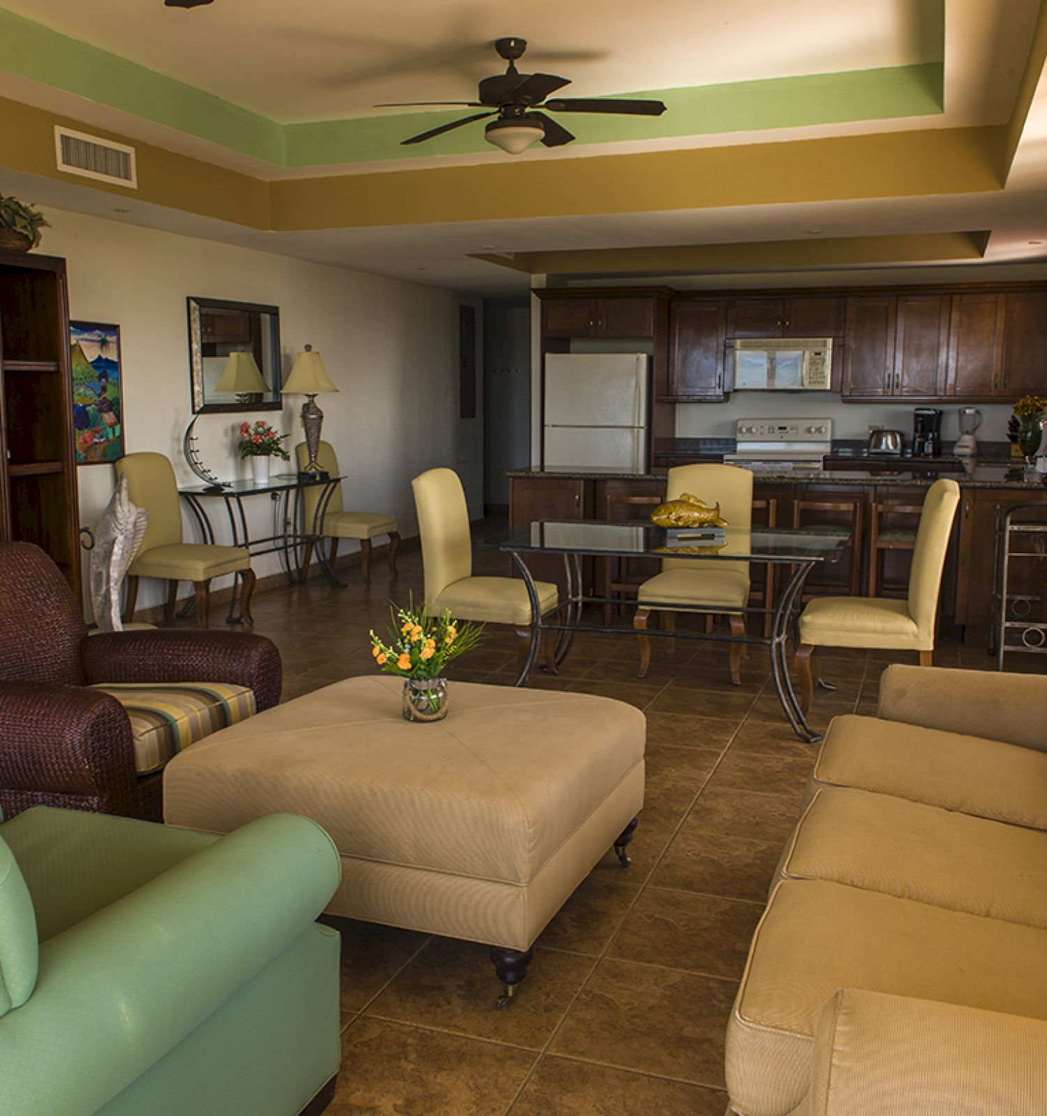 A cozy living room features various sofas, armchairs, a TV, and a dining area with a kitchen in the background, decorated with warm lighting.