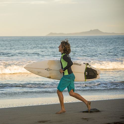 A person is running on the beach holding a surfboard, with waves crashing in the background and an island visible in the distance, ending the sentence.