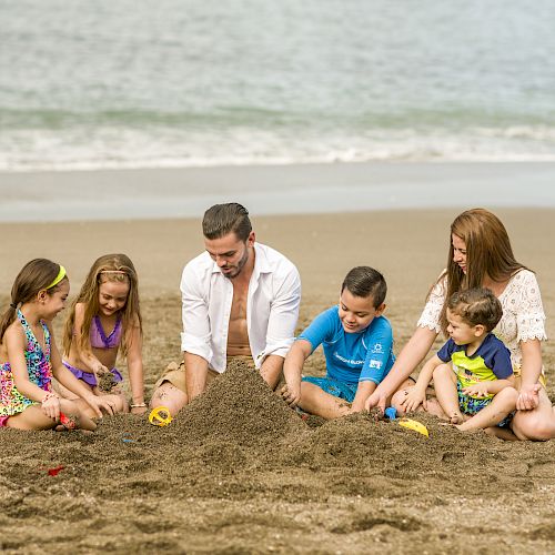 A family of six, consisting of four children and two adults, is playing in the sand at the beach near the water.