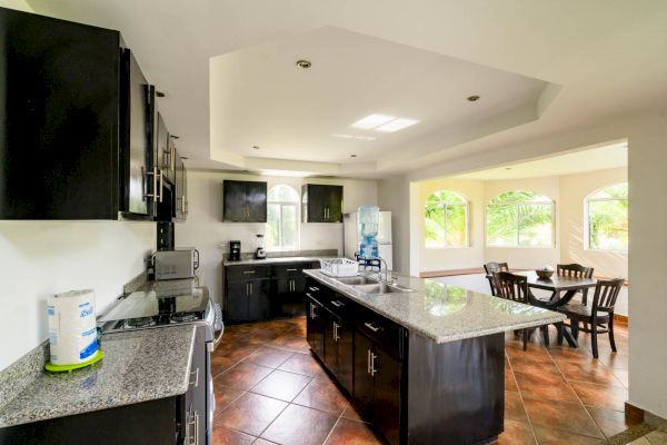 A spacious kitchen with dark cabinets, granite countertops, and stainless steel appliances. An adjacent dining area with windows and a wooden table.