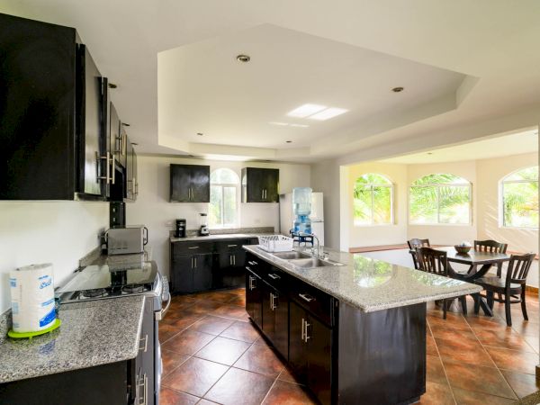 A spacious kitchen with dark cabinets, granite countertops, and stainless steel appliances. An adjacent dining area with windows and a wooden table.