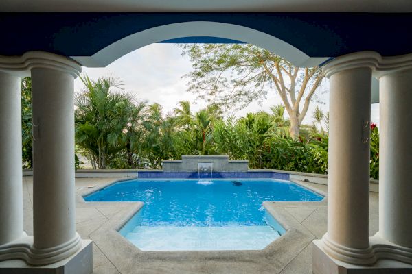 This image shows a luxurious outdoor pool area with columns, tropical plants, and a serene ambiance.