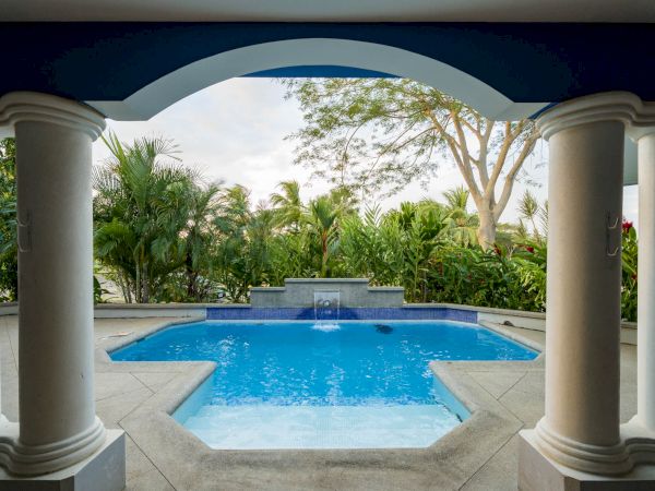 This image shows a luxurious outdoor pool area with columns, tropical plants, and a serene ambiance.