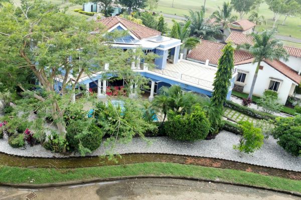 An aerial view of a spacious, landscaped property with multiple buildings, a large tree, and a manicured garden surrounded by lush greenery.