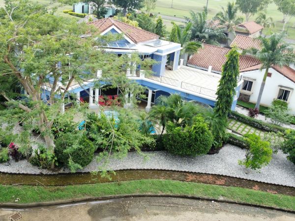 An aerial view of a spacious, landscaped property with multiple buildings, a large tree, and a manicured garden surrounded by lush greenery.