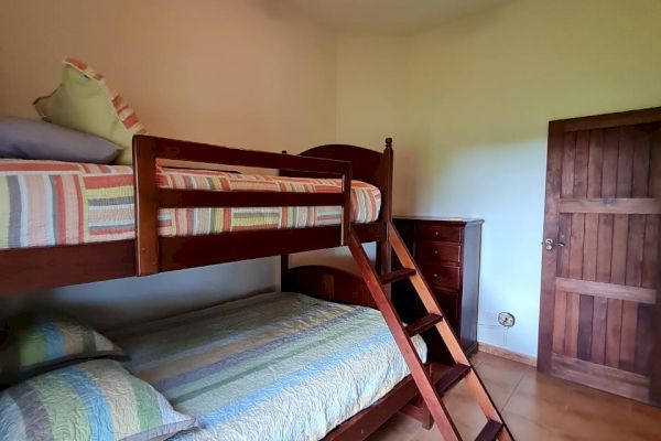 The image shows a room with a bunk bed, wooden ladder, ceiling fan with light, and a wooden door. Pillows and striped bedding are visible.