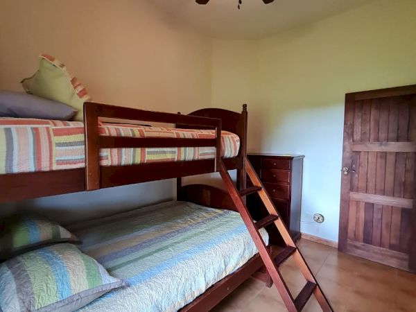 The image shows a room with a bunk bed, wooden ladder, ceiling fan with light, and a wooden door. Pillows and striped bedding are visible.