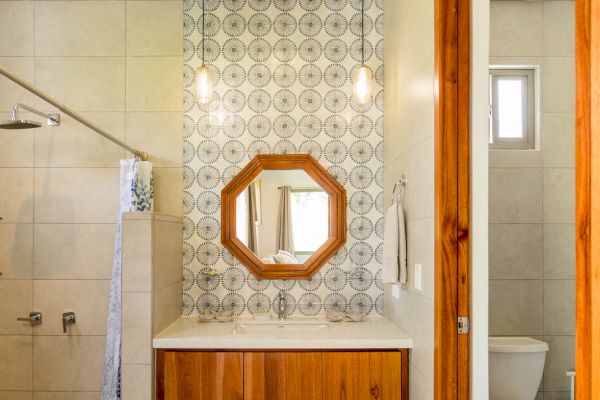 Modern bathroom with a vanity, wooden accents, a patterned backsplash, an octagonal mirror, a shower area, and a separate toilet space.