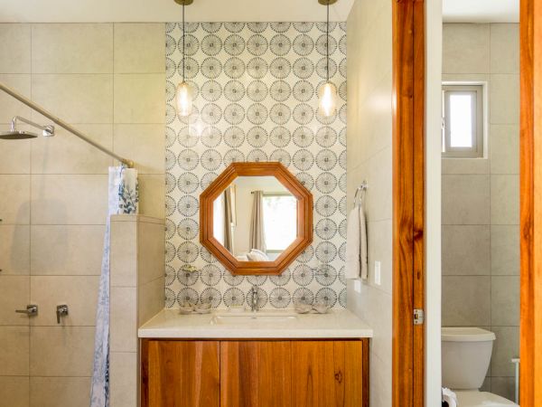 Modern bathroom with a vanity, wooden accents, a patterned backsplash, an octagonal mirror, a shower area, and a separate toilet space.