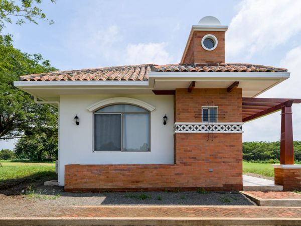 A small, single-story house with a combination of white and brick walls, surrounded by green grass and trees, under a clear sky ending the sentence.