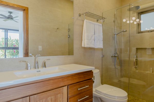 A modern bathroom with wooden cabinets, a large mirror, a toilet, and a glass-enclosed shower with towels on a rack.