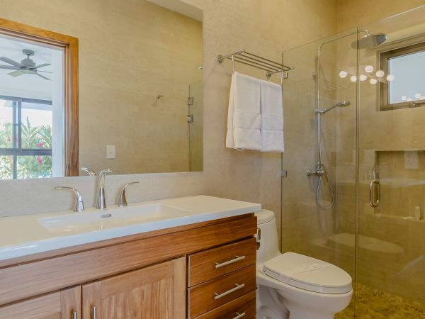 A modern bathroom with wooden cabinets, a large mirror, a toilet, and a glass-enclosed shower with towels on a rack.