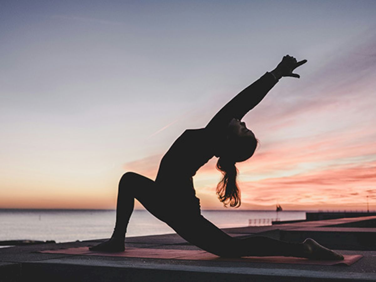 A person practices yoga in a lunge position on a rooftop at sunset, with the sky displaying vibrant hues.