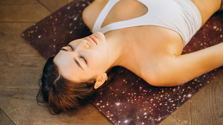 A person is lying relaxed on a yoga mat with eyes closed, surrounded by candles and incense, creating a serene atmosphere.