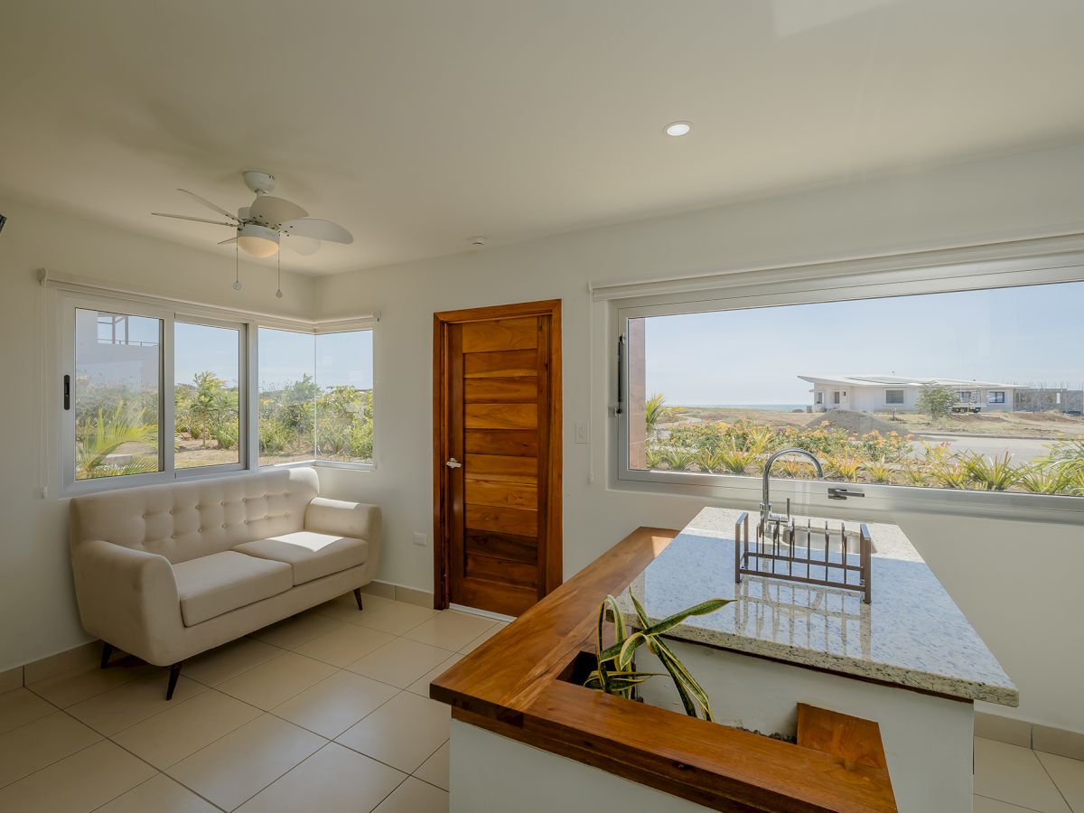 A cozy room features a sofa, wooden door, and large windows with a scenic view. A countertop island with a plant adds to the inviting atmosphere.