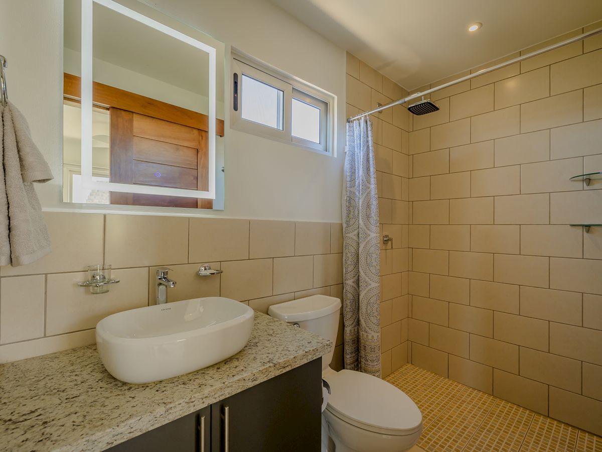 The image shows a modern bathroom with a granite countertop, a vessel sink, a toilet, a walk-in shower with a curtain, and beige tiles.