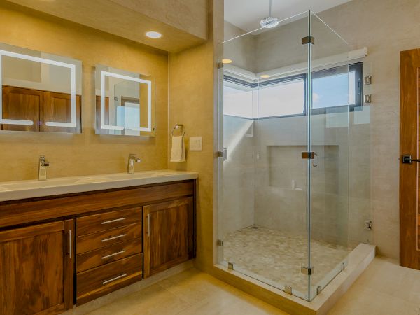 The image shows a modern bathroom with a wooden vanity, two illuminated mirrors, and a glass-enclosed shower area with a window.