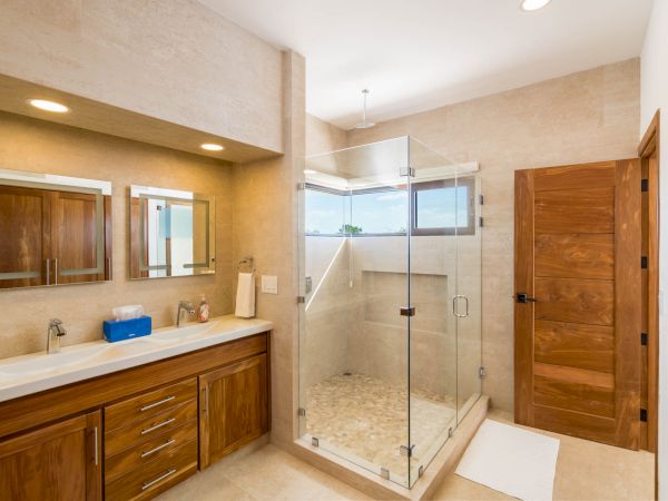 This image shows a modern bathroom with a double vanity, wooden cabinets, and a glass-enclosed shower area.