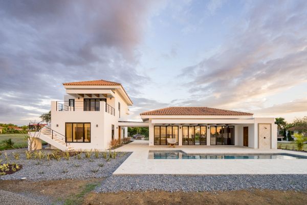 A modern two-story house with large windows, a balcony, and a swimming pool in the front yard, surrounded by a well-maintained garden.