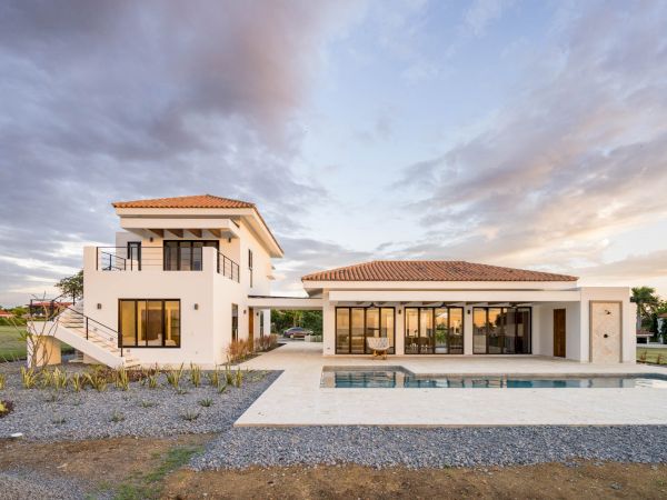 A modern two-story house with large windows, a balcony, and a swimming pool in the front yard, surrounded by a well-maintained garden.