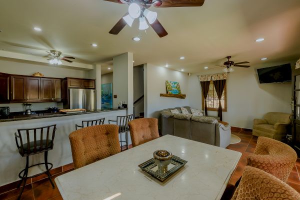 A cozy open-concept living space with a kitchen, dining area, and living room; brown and beige decor, ceiling fans, and modern furnishings.