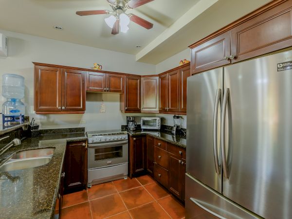 This image shows a modern kitchen with wooden cabinets, stainless steel appliances, and a ceiling fan. There is a water dispenser on the countertop.