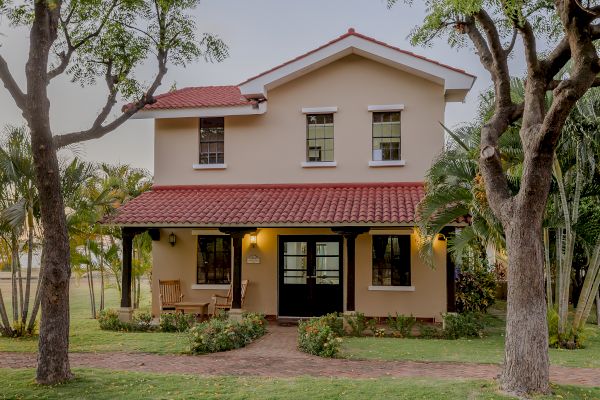 The image shows a two-story house with a red-tiled roof, surrounded by trees and greenery, and a well-maintained lawn in the front yard.