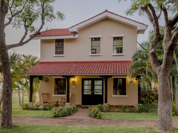 The image shows a two-story house with a red-tiled roof, surrounded by trees and greenery, and a well-maintained lawn in the front yard.