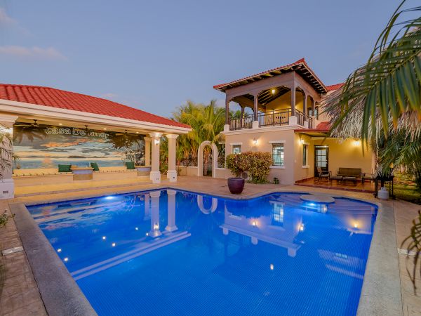 A luxurious villa with a swimming pool, surrounded by tropical plants, featuring an outdoor lounge area with seating and a decorative mural.