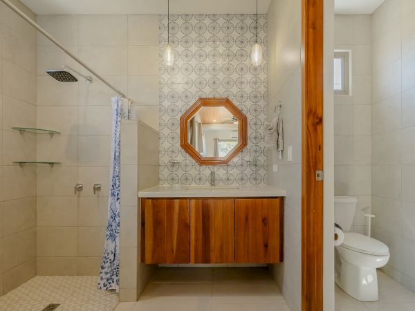 A modern bathroom with a walk-in shower, a wood-accented vanity with a round mirror, and a toilet on the right side of the room.