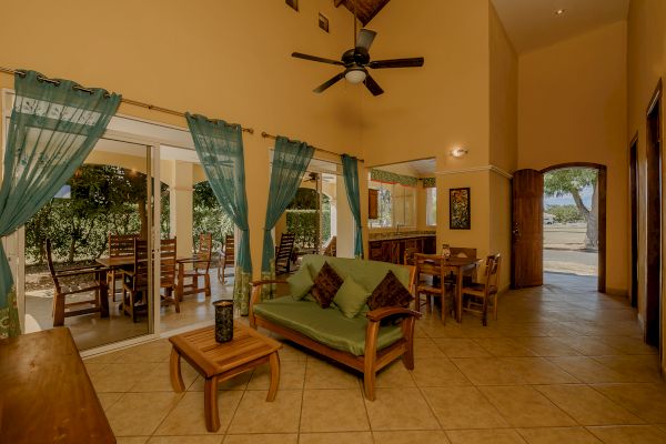 A cozy living area with tall ceilings, a green sofa, wooden furniture, teal curtains, and a view of an outdoor seating patio.