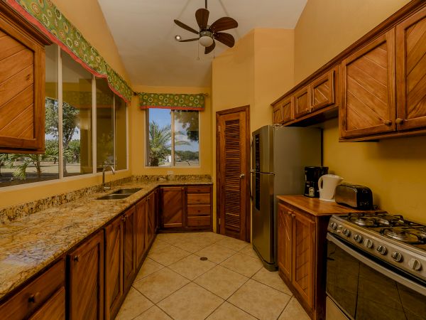 A kitchen featuring wooden cabinets, granite countertops, a refrigerator, a stove, a kettle, a toaster, a ceiling fan, and windows with a scenic view.