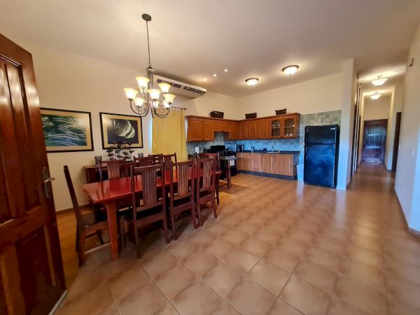 A spacious kitchen and dining area featuring wooden furniture, a chandelier, wall art, and appliances such as a refrigerator and stove.
