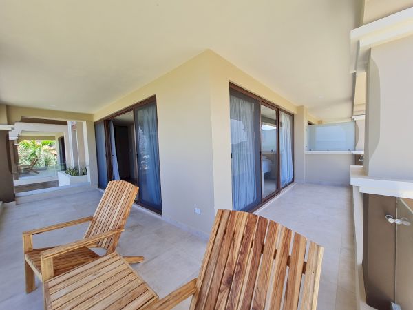 The image shows a patio area with wooden chairs, large sliding glass doors, and light-colored walls, giving a clean, modern, and open appearance.