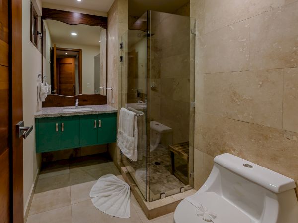 The image shows a bathroom with a green vanity, a sink, a glass-enclosed shower, and a white toilet. There's a towel and a folded mat on the floor.