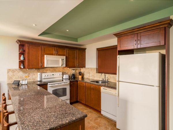 A modern kitchen with wooden cabinets, granite countertop, white appliances including a refrigerator, oven, microwave, and a small dining area.