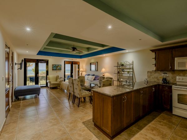 A spacious living area with a kitchen on the right, and dining and seating areas leading to a balcony with a view.