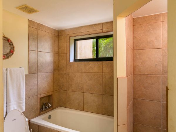 A bathroom with a toilet, bathtub, window, towel, and a walk-in shower with beige tiles and yellow walls is shown.
