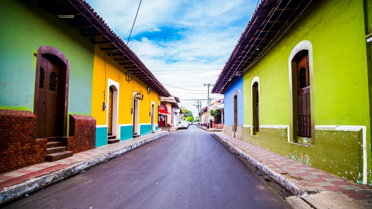A vibrant street with colorful houses on both sides, featuring green, yellow, and blue exteriors, and a clear sky overhead.