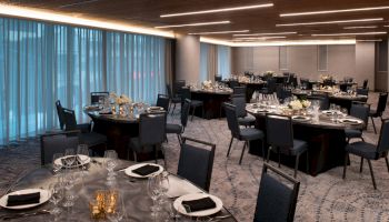 The image shows an elegant banquet hall set with round tables, black chairs, candles, and white floral centerpieces, ready for a formal event.