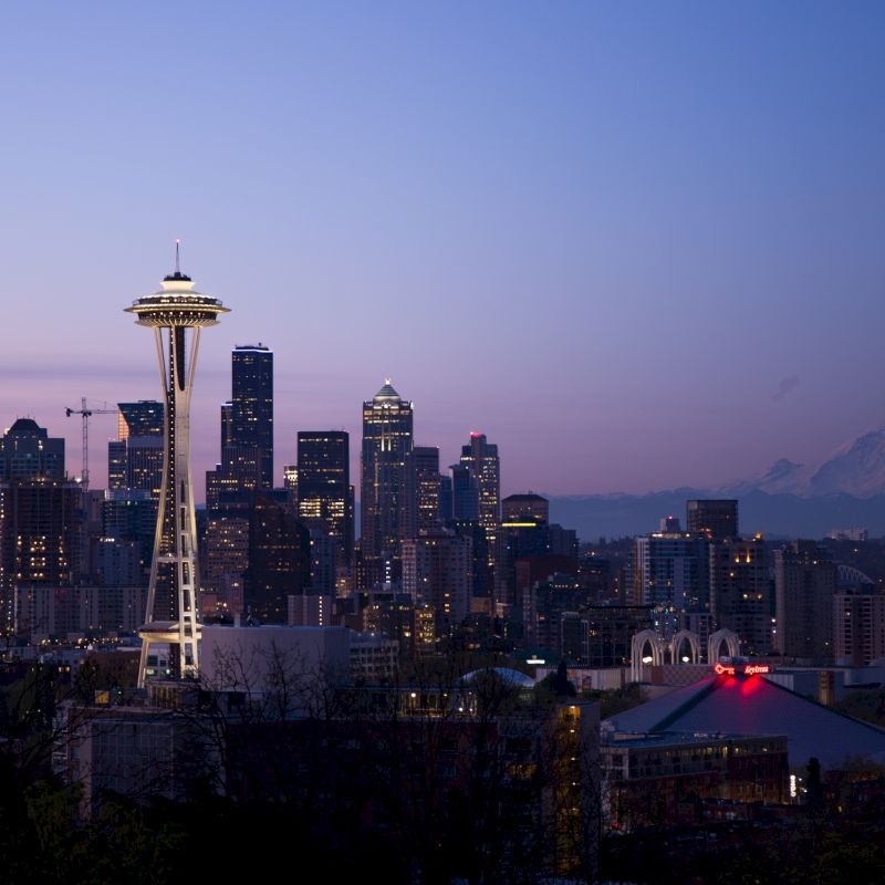 This image shows a city skyline at dusk with notable landmarks, including the Space Needle, and a mountain in the background, likely Mount Rainier.