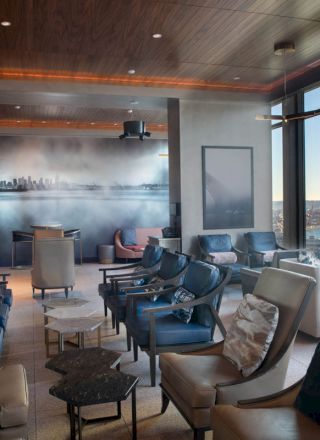 A modern lounge area with plush seating, large windows offering a city and water view, a wall mural, and elegant decor can be seen in this image.