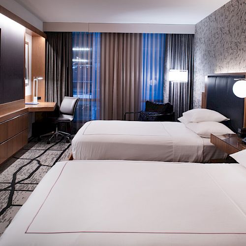 A modern hotel room with two double beds, a flat-screen TV, a desk with a chair, and contemporary decor ending the sentence.